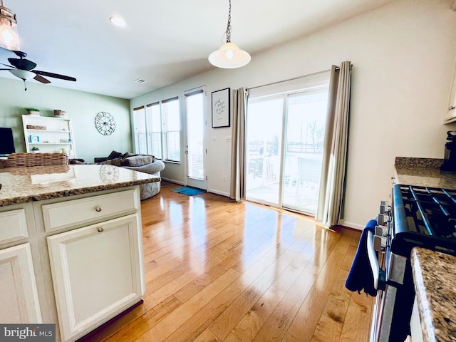 kitchen with decorative light fixtures, light wood-style floors, open floor plan, white cabinets, and stainless steel gas range oven