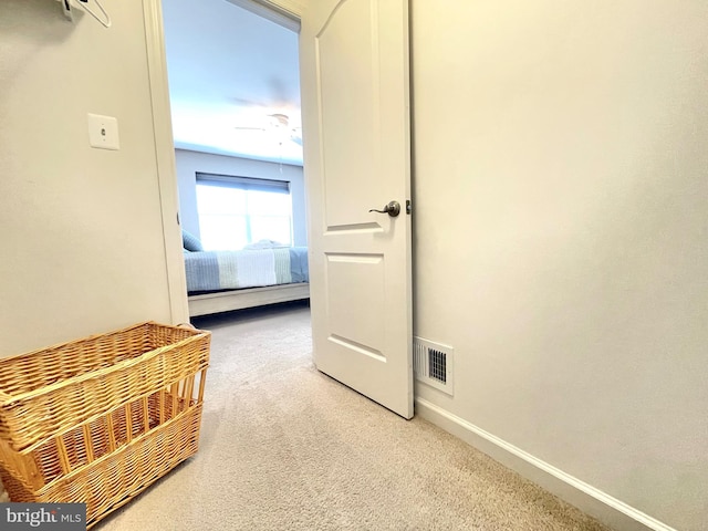 hallway with light carpet, visible vents, and baseboards