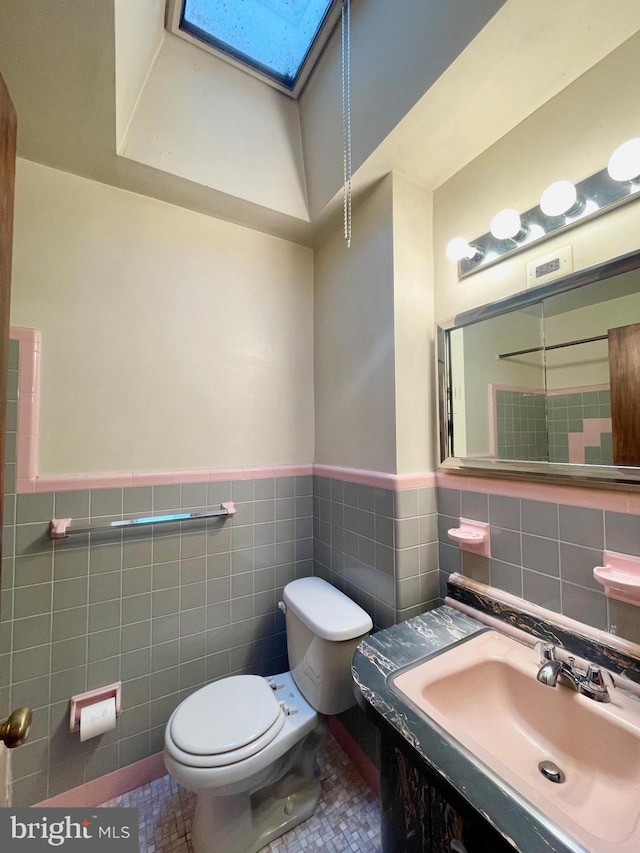 half bath with toilet, a skylight, tile walls, and wainscoting