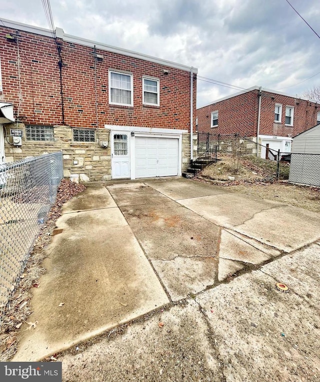 back of house featuring brick siding, concrete driveway, an attached garage, fence, and stone siding