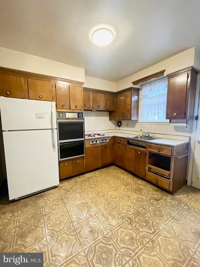 kitchen with a sink, light countertops, freestanding refrigerator, a warming drawer, and cooktop