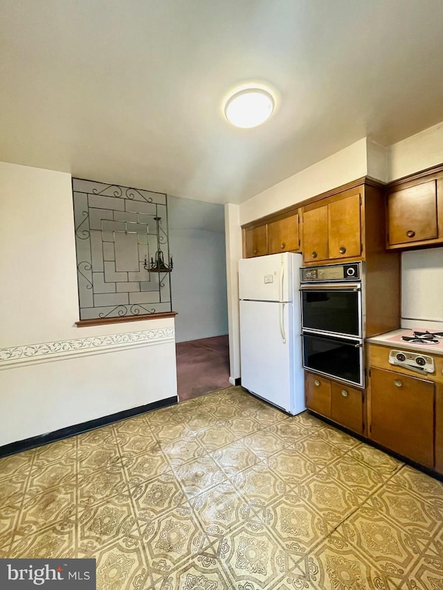 kitchen featuring a warming drawer, cooktop, light countertops, brown cabinetry, and freestanding refrigerator