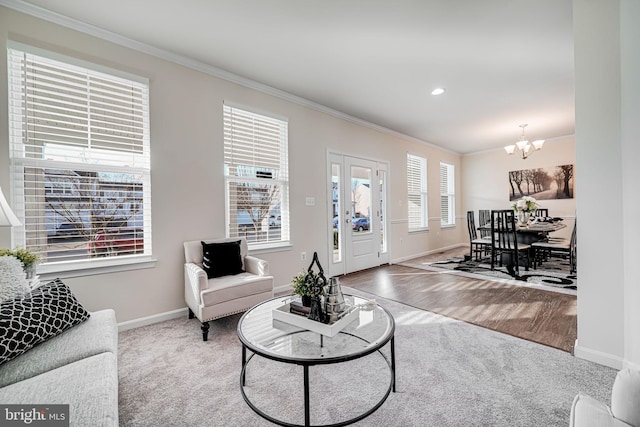 living area with baseboards, a chandelier, crown molding, and wood finished floors