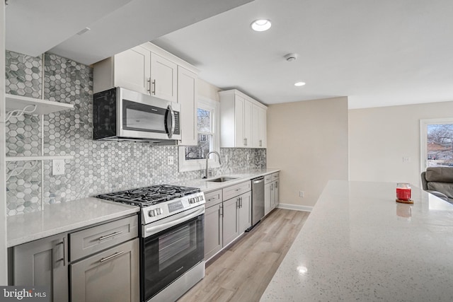 kitchen with tasteful backsplash, light stone countertops, stainless steel appliances, open shelves, and a sink