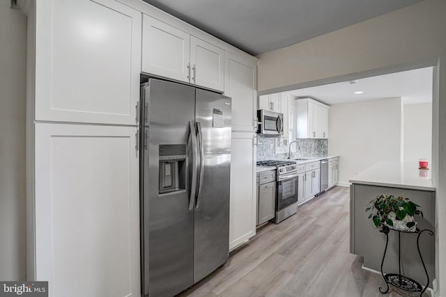 kitchen featuring light wood-style flooring, stainless steel appliances, a sink, light countertops, and decorative backsplash