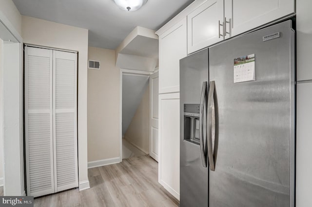 kitchen with visible vents, light wood-style floors, white cabinetry, stainless steel fridge, and baseboards