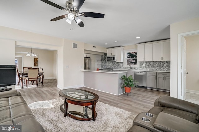 living room featuring light wood-style floors, baseboards, visible vents, and ceiling fan