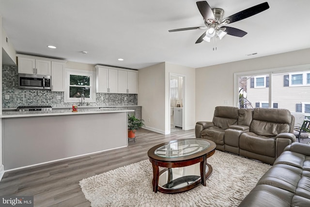 living room featuring a ceiling fan, baseboards, wood finished floors, and recessed lighting