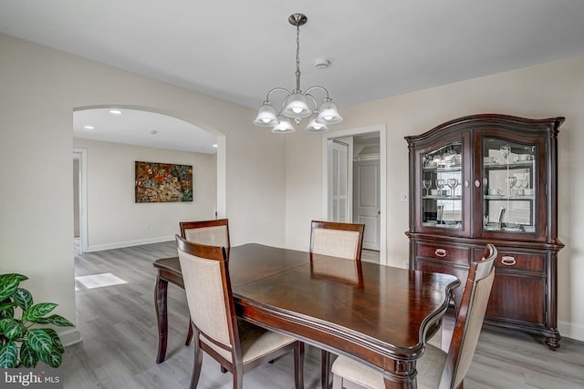 dining room with light wood-type flooring, arched walkways, baseboards, and an inviting chandelier