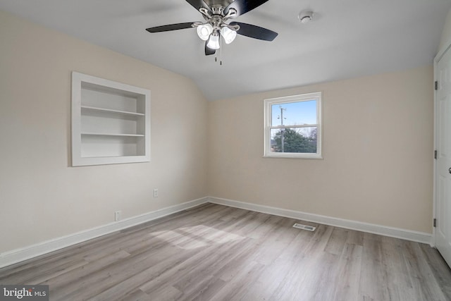 empty room featuring built in features, lofted ceiling, visible vents, wood finished floors, and baseboards