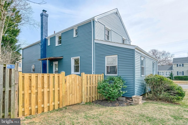 view of side of home featuring a chimney, fence, and a yard