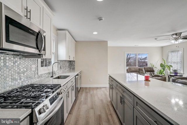 kitchen featuring light wood finished floors, stainless steel appliances, tasteful backsplash, open floor plan, and a sink