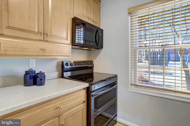 kitchen featuring light brown cabinets, black microwave, and range with two ovens