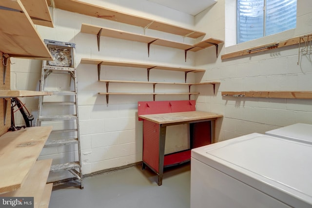 clothes washing area with laundry area, a workshop area, washer and clothes dryer, and concrete block wall