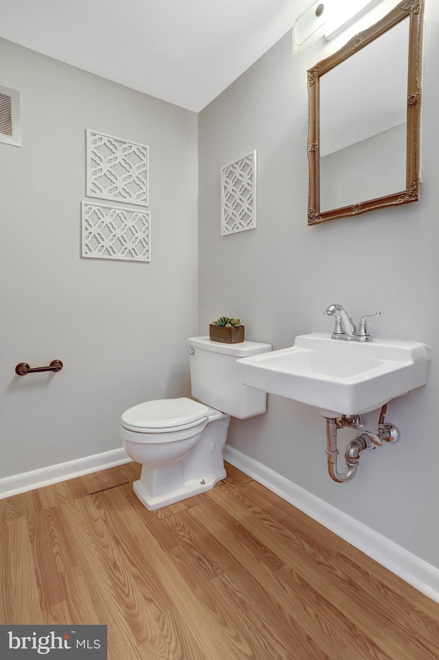 half bathroom featuring visible vents, baseboards, toilet, wood finished floors, and a sink