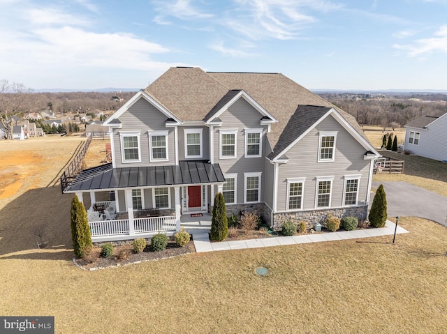 view of front of property featuring a porch, a shingled roof, stone siding, a standing seam roof, and a front yard