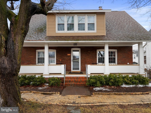 view of front of house featuring covered porch, brick siding, and roof with shingles