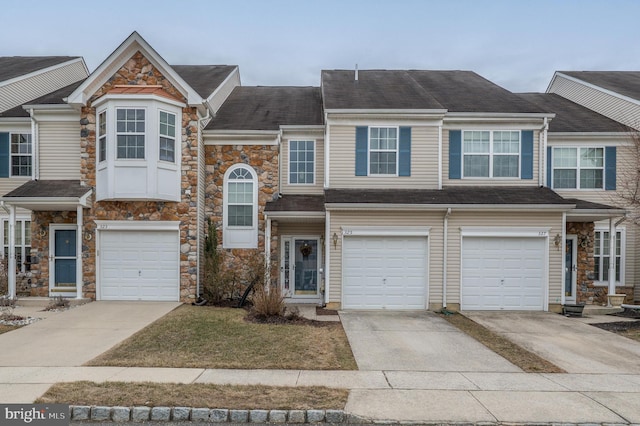 multi unit property with an attached garage, driveway, and stone siding