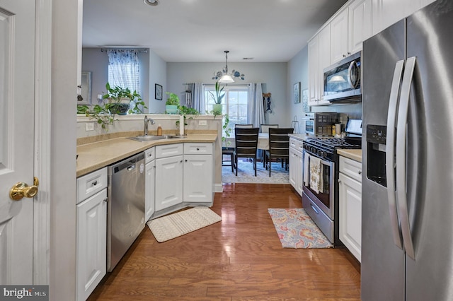 kitchen with stainless steel appliances, light countertops, white cabinets, a sink, and a peninsula