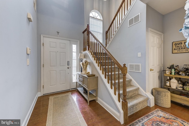 foyer with a towering ceiling, wood finished floors, visible vents, and baseboards