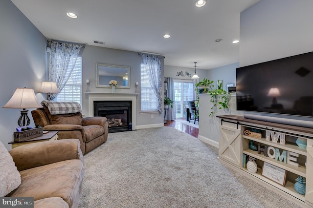 carpeted living room with a fireplace with flush hearth, visible vents, baseboards, and recessed lighting