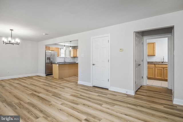 unfurnished living room with a chandelier, baseboards, light wood-style floors, and a sink