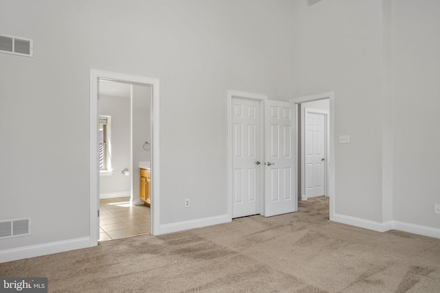 unfurnished bedroom with carpet, visible vents, a towering ceiling, and baseboards