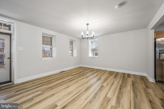 unfurnished dining area with light wood finished floors, a notable chandelier, visible vents, and baseboards