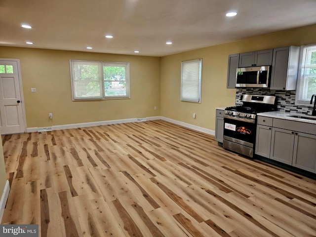 kitchen with gray cabinets, backsplash, light wood-style flooring, appliances with stainless steel finishes, and a sink