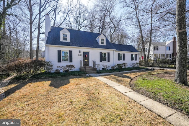 cape cod home with brick siding, a chimney, fence, and a front yard