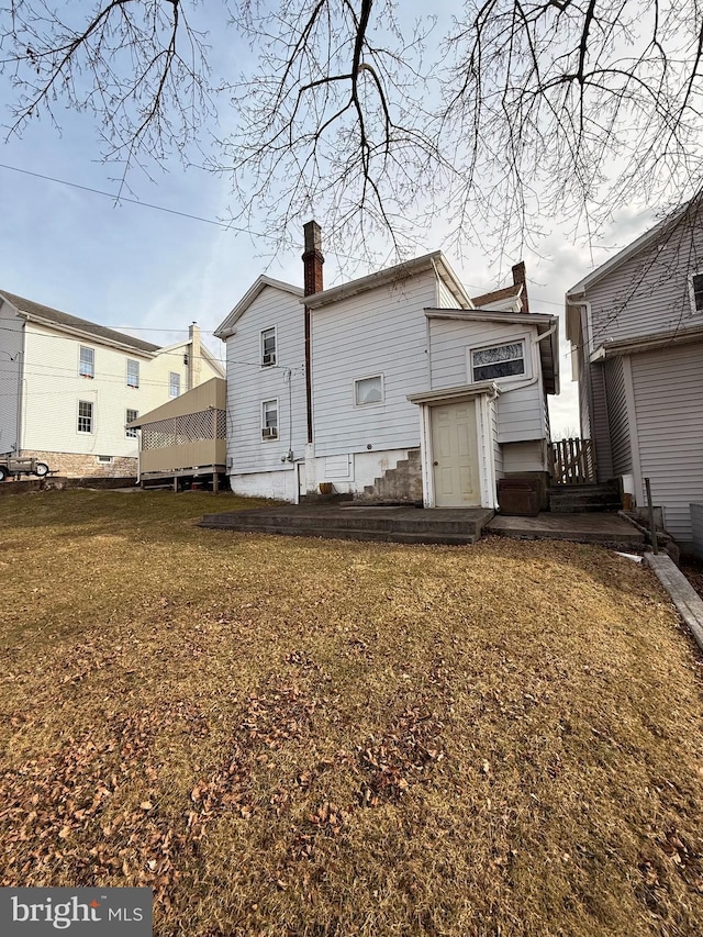 rear view of house featuring a chimney and a lawn