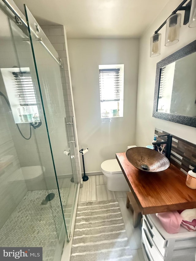 bathroom featuring a stall shower, a sink, toilet, and baseboards