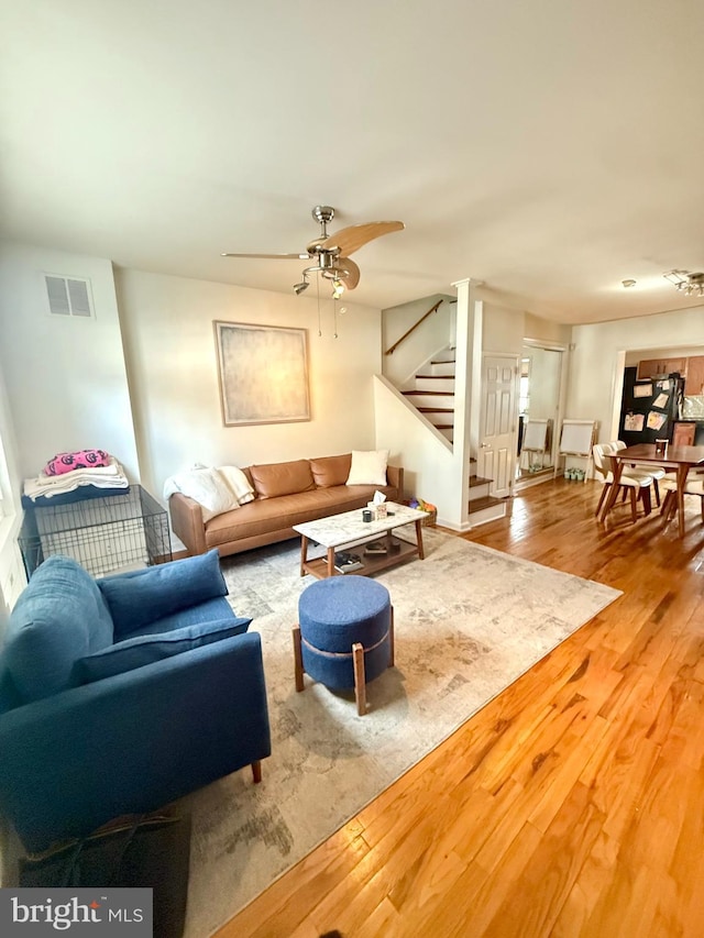 living room with stairway, wood finished floors, visible vents, and a ceiling fan