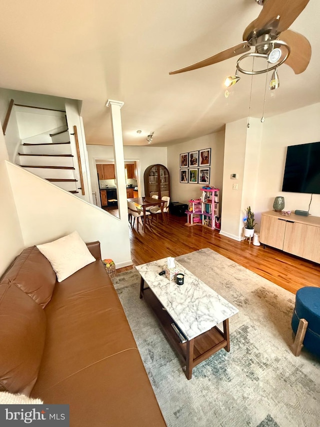 living area with a ceiling fan, wood finished floors, decorative columns, and stairs