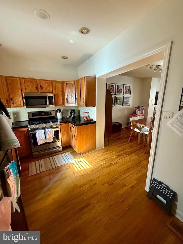 kitchen featuring stainless steel appliances, light wood finished floors, brown cabinetry, and dark countertops