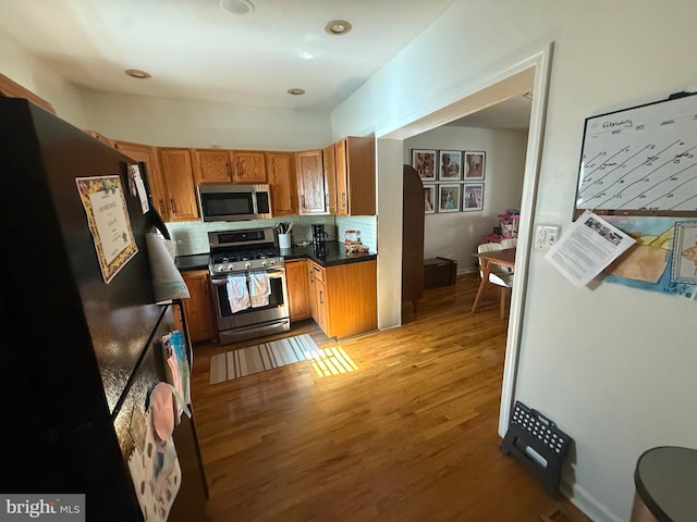 kitchen with stainless steel appliances, light wood-type flooring, brown cabinets, tasteful backsplash, and dark countertops