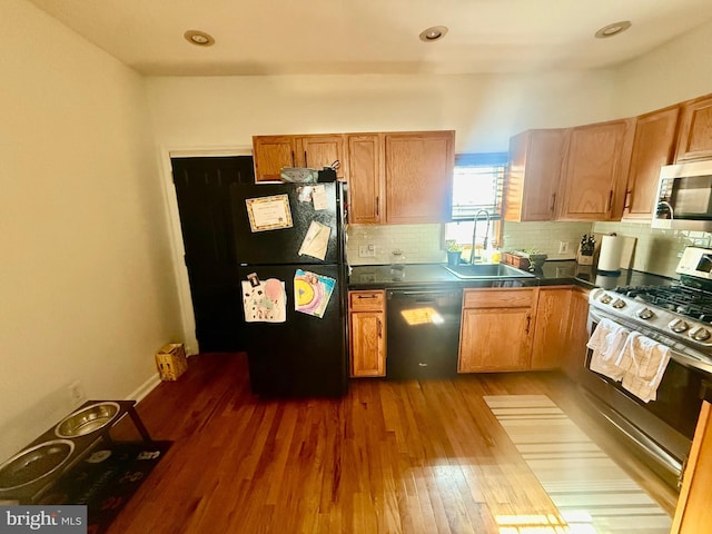 kitchen featuring decorative backsplash, dark countertops, wood finished floors, black appliances, and a sink