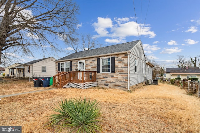 single story home featuring cooling unit, stone siding, and fence