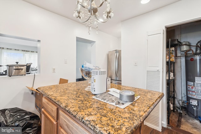 kitchen featuring a chandelier, water heater, light stone counters, freestanding refrigerator, and brown cabinetry