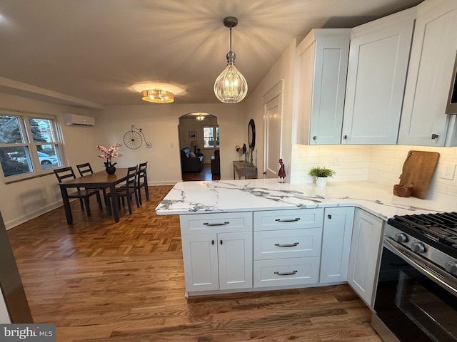 kitchen with stainless steel gas stove, arched walkways, decorative backsplash, a peninsula, and a wall mounted AC