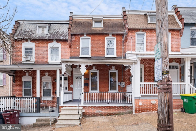 multi unit property with a shingled roof, mansard roof, a porch, and brick siding