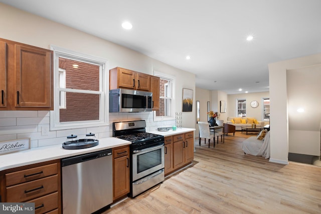 kitchen featuring light wood-style flooring, stainless steel appliances, backsplash, and light countertops