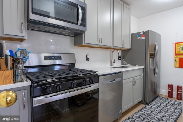 kitchen with stainless steel appliances, light countertops, backsplash, a sink, and light wood-type flooring