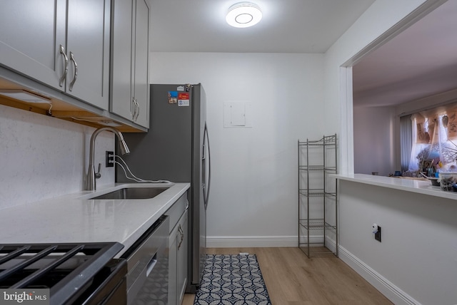 kitchen with gray cabinetry, a sink, baseboards, light wood-style floors, and light countertops