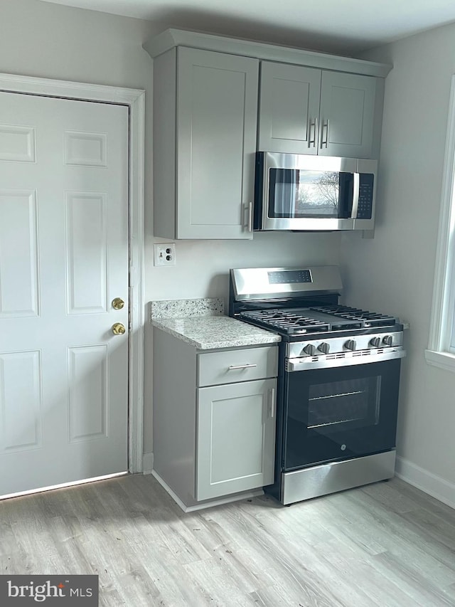 kitchen with gray cabinetry, appliances with stainless steel finishes, light stone countertops, and light wood-style floors