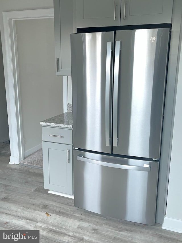 kitchen with light wood finished floors, gray cabinets, freestanding refrigerator, light stone countertops, and baseboards