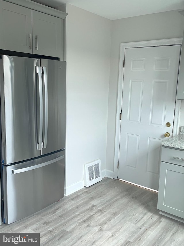 kitchen featuring light stone counters, light wood-style flooring, visible vents, baseboards, and freestanding refrigerator