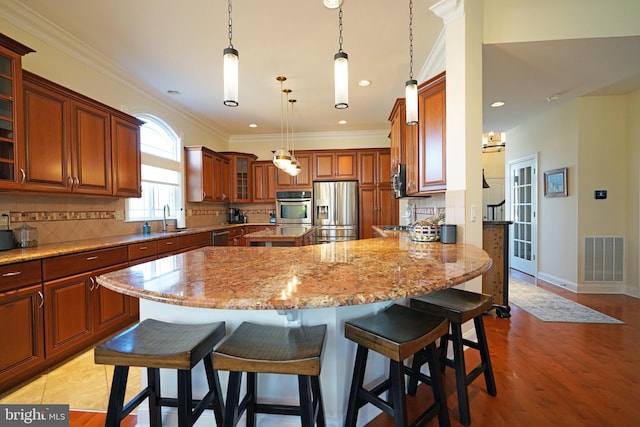 kitchen with visible vents, a kitchen breakfast bar, light stone countertops, stainless steel appliances, and a sink