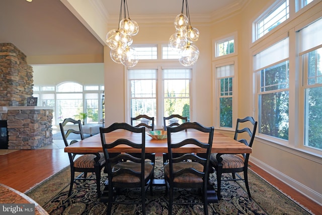 dining space with baseboards, a fireplace, wood finished floors, and crown molding