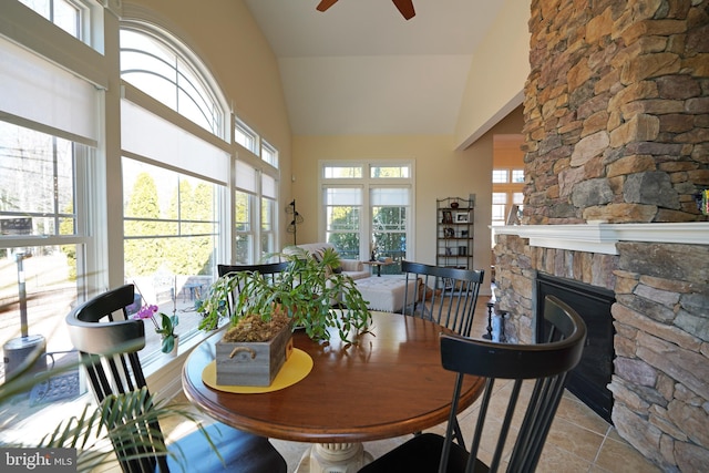 tiled dining room with high vaulted ceiling, ceiling fan, and a stone fireplace